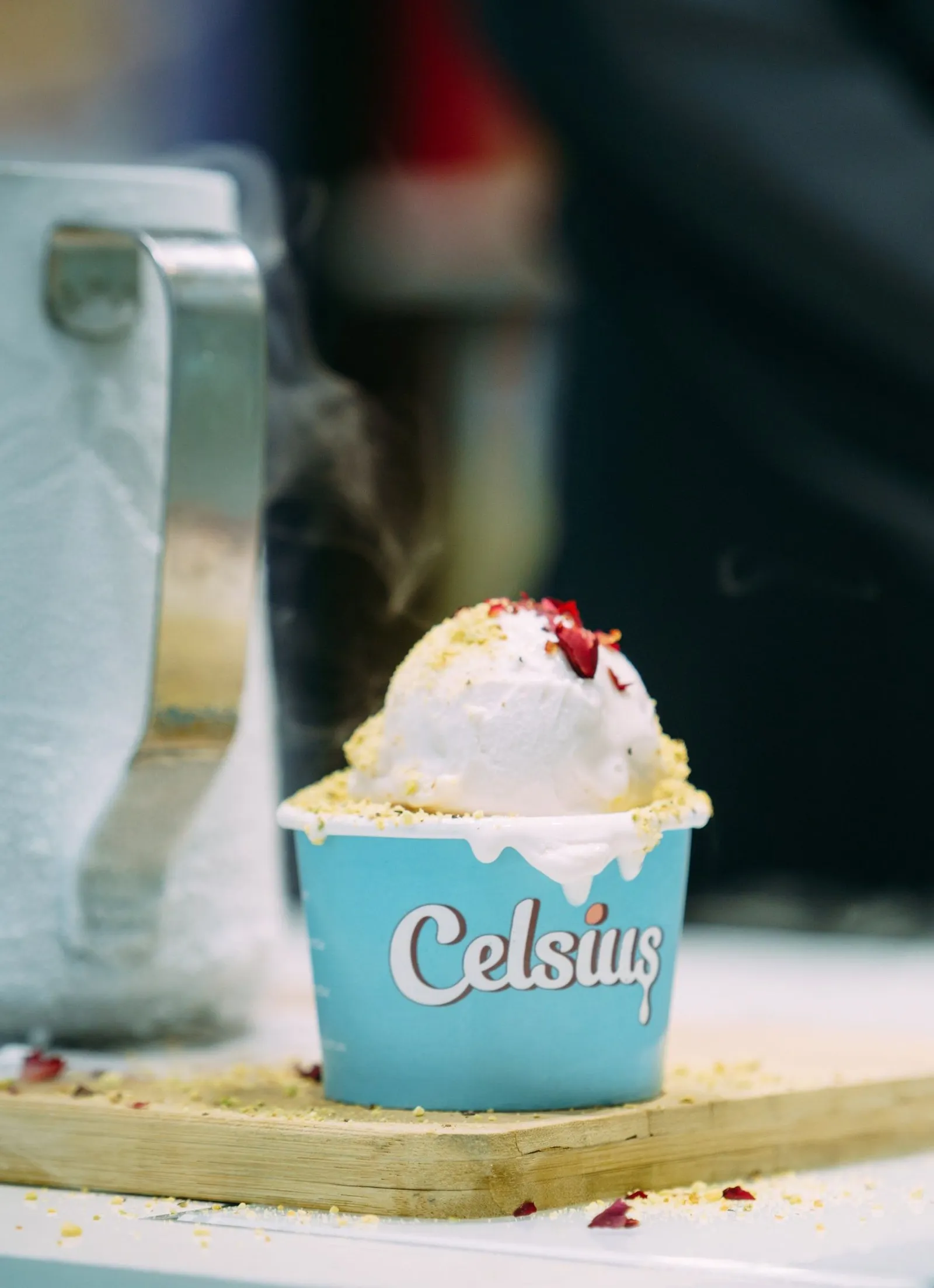 A scoop of gelato in a Celsius cup, topped with crushed pistachio and rose petals