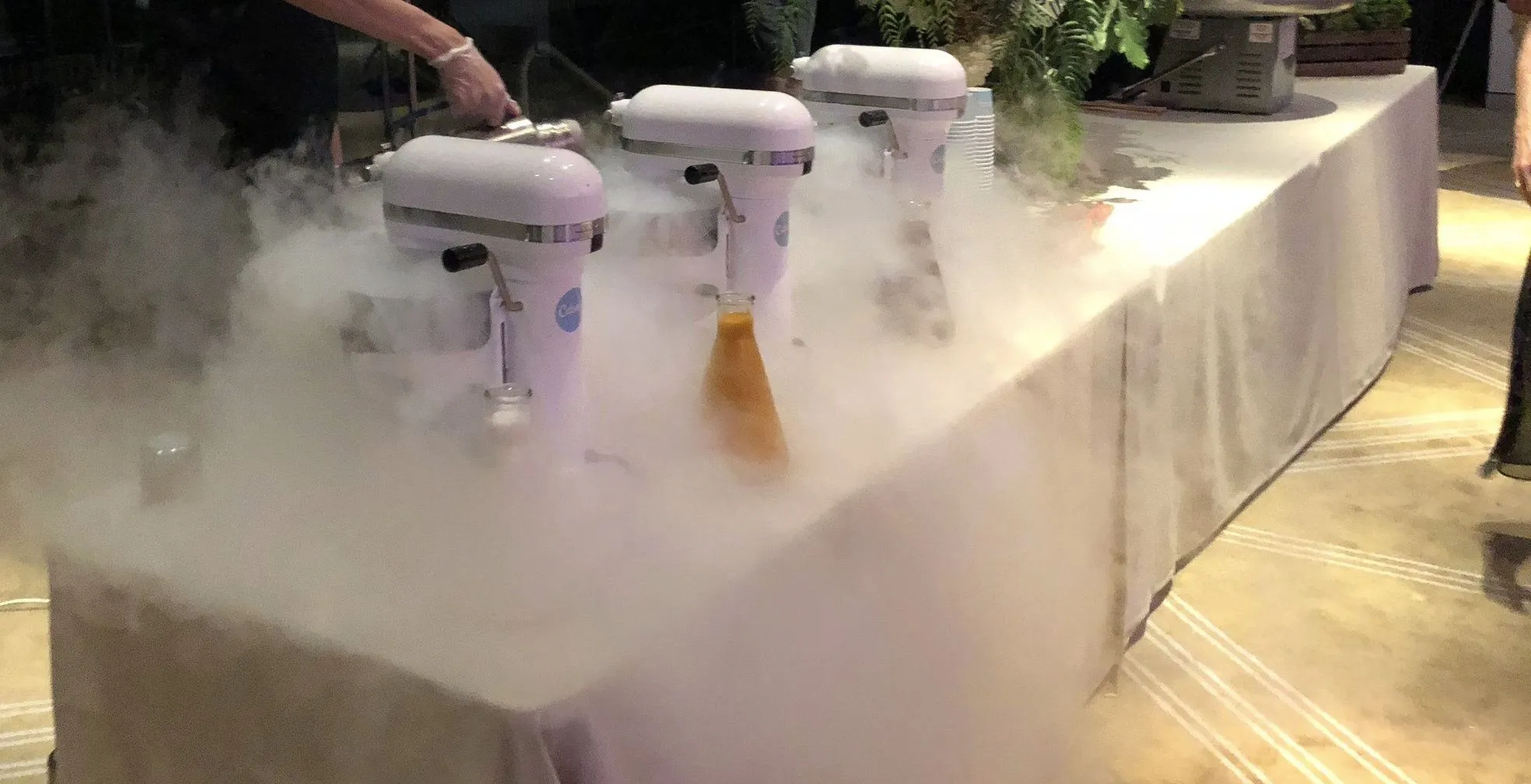 Three mixers on a linen-covered table at an evening event, nitrogen fog rolling across the table and over its edge
