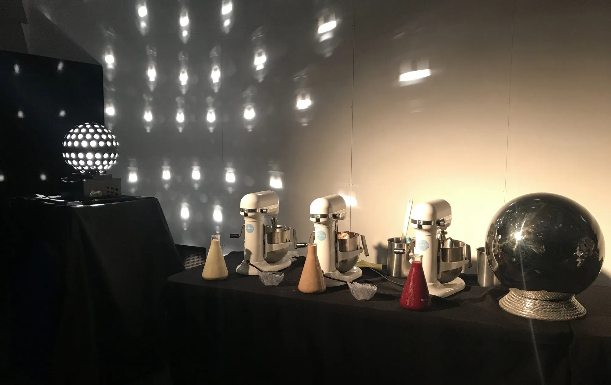 Three mixers and flasks of gelato base on a black table, lit by a mirror ball